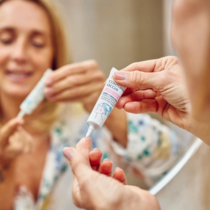 Donna allo specchio applica sul dito il siero contorno occhi